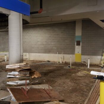 A large empty room with exposed brick, tall pillars, exposed flooring and upside down wooden tables.