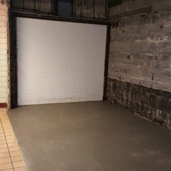 Interior of an empty room with exposed brick, tiled walls and a cement floor.