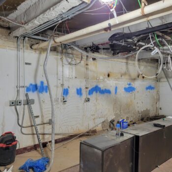 Interior of a construction site with cement walls, blue spray paint and cables hanging above the roof.