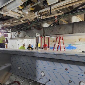 A construction site with workers in hardhats in the background. A ladder is behind an unfinished counter.