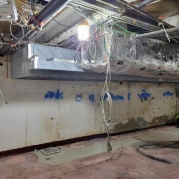 Interior of a construction site with blue spray paint on the cement walls, an wires hanging from the ceiling.