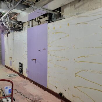Interior of a construction site with a purple panel in the middle. Old dried glue can be seen on the walls.
